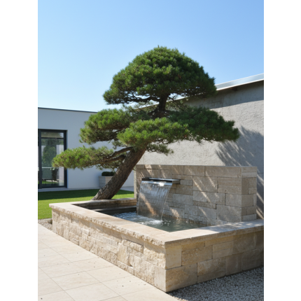Exklusives modernes Wasserspiel aus Naturstein mit integriertem Edelstahl-Wasserfall auf einer minimalistischen Terrasse vor moderner Architektur